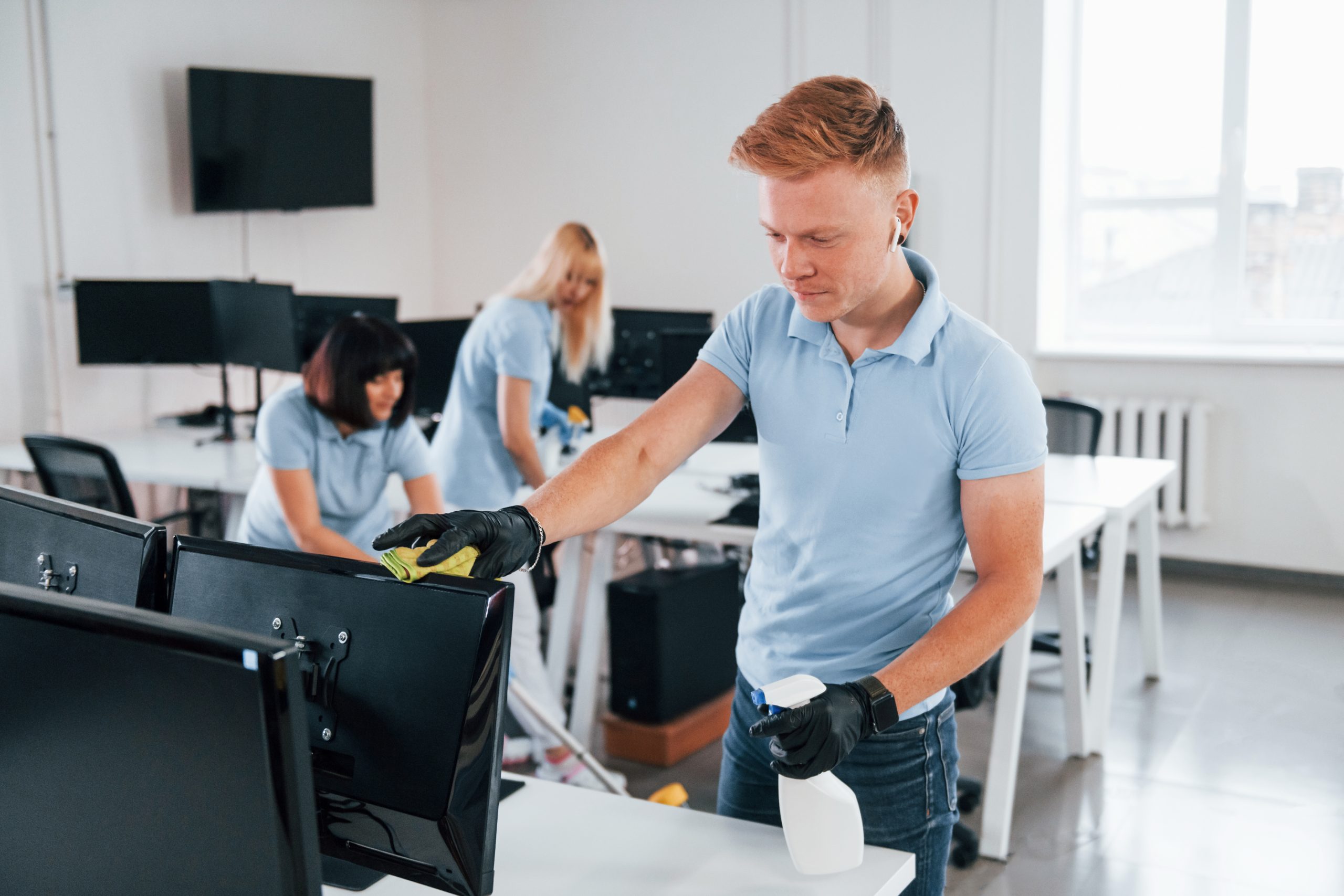 Cleans monitor. Group of workers clean modern office together at daytime.