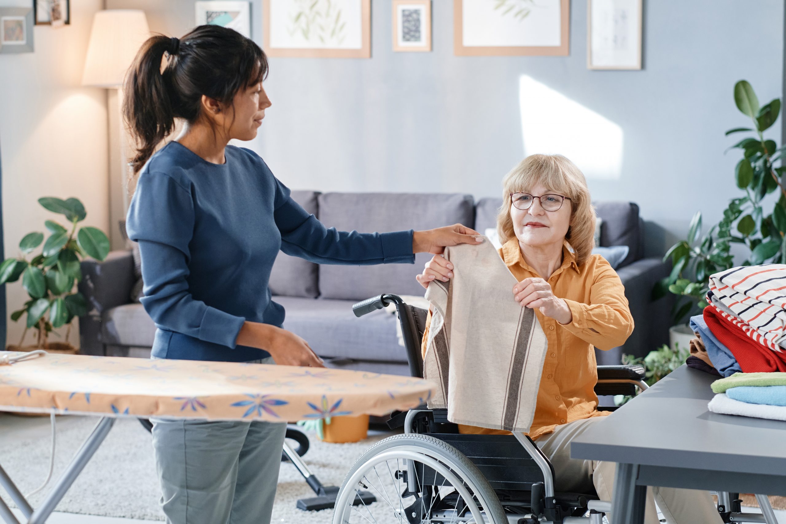 Housekeeper helping to iron the clothes to senior woman who using wheelchair at home